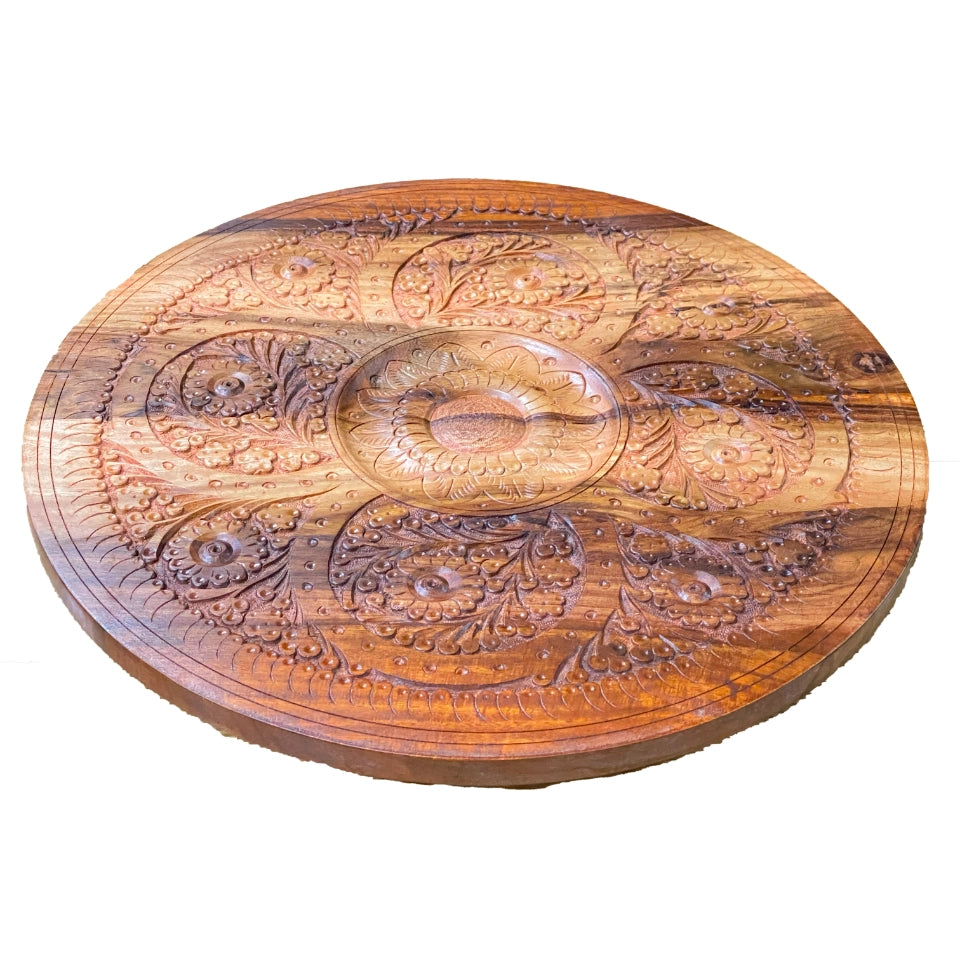 Handcrafted wooden pedestal table with intricate carved floral and paisley motifs covering the round tabletop and circular base, featuring a turned wooden pedestal stem with traditional carved details